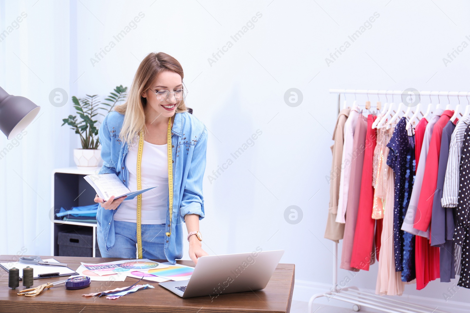 Photo of Beautiful young stylist at workplace near rack with clothes. Space for text