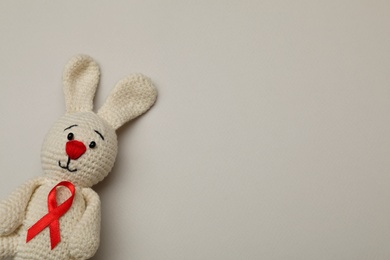 Photo of Cute knitted toy bunny with red ribbon on beige background, top view and space for text. AIDS disease awareness