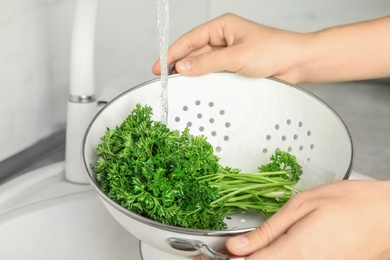 Photo of Woman washing fresh parsley in colander under tap water, closeup