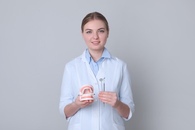 Photo of Dental assistant holding jaws model and tools on light grey background