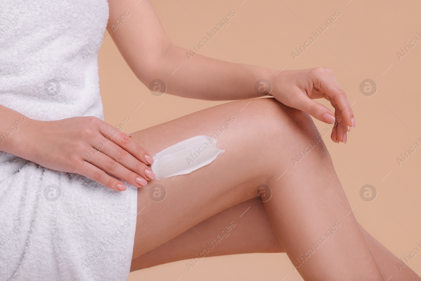 Photo of Woman with smear of body cream on her leg against light brown background, closeup