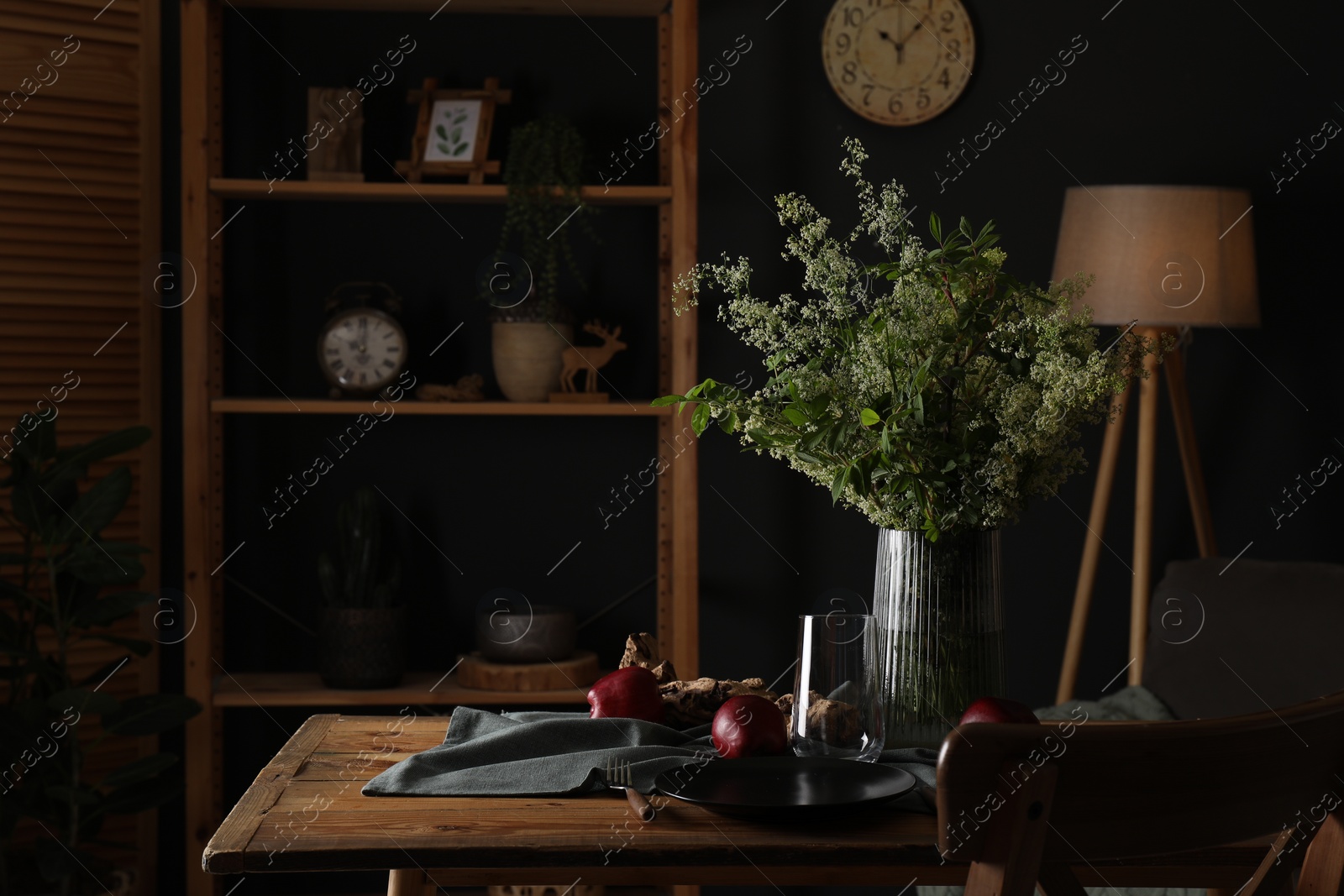 Photo of Set of clean dishware, ripe red apples and flowers on wooden table in stylish dining room