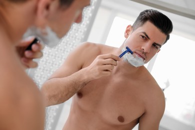 Photo of Handsome man shaving near mirror in bathroom