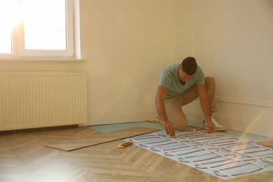 Professional worker installing electric underfloor heating system indoors