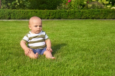 Photo of Adorable little baby sitting on green grass outdoors