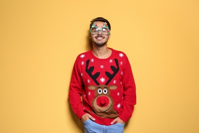 Photo of Young man in Christmas sweater with party glasses on color background