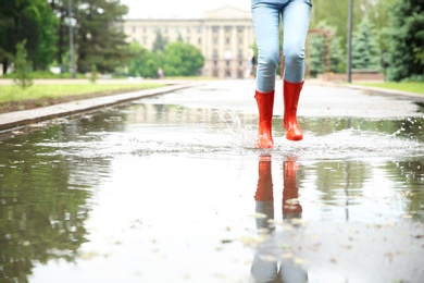 Woman with red rubber boots jumping in puddle, closeup. Rainy weather