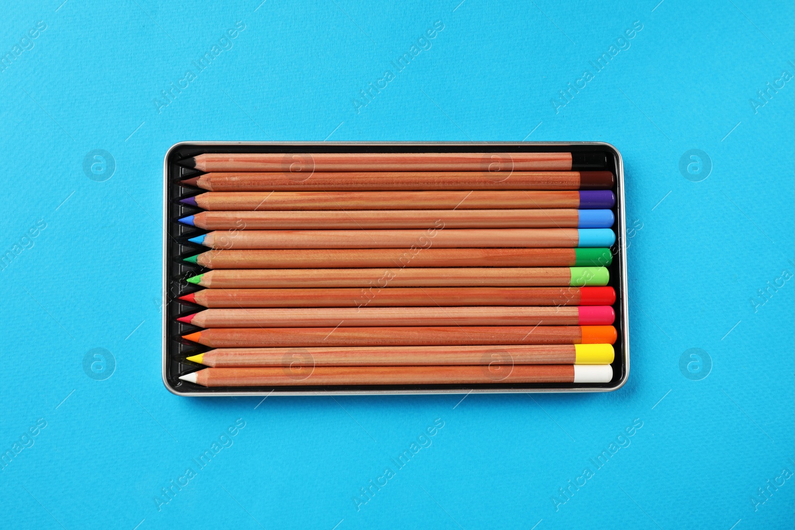 Photo of Box with many colorful pastel pencils on light blue background, top view. Drawing supplies