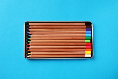Box with many colorful pastel pencils on light blue background, top view. Drawing supplies