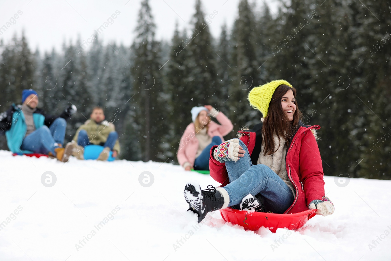 Photo of Happy friends sliding on sleds outdoors. Winter vacation