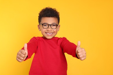 Photo of African-American boy with glasses showing thumbs up on yellow background