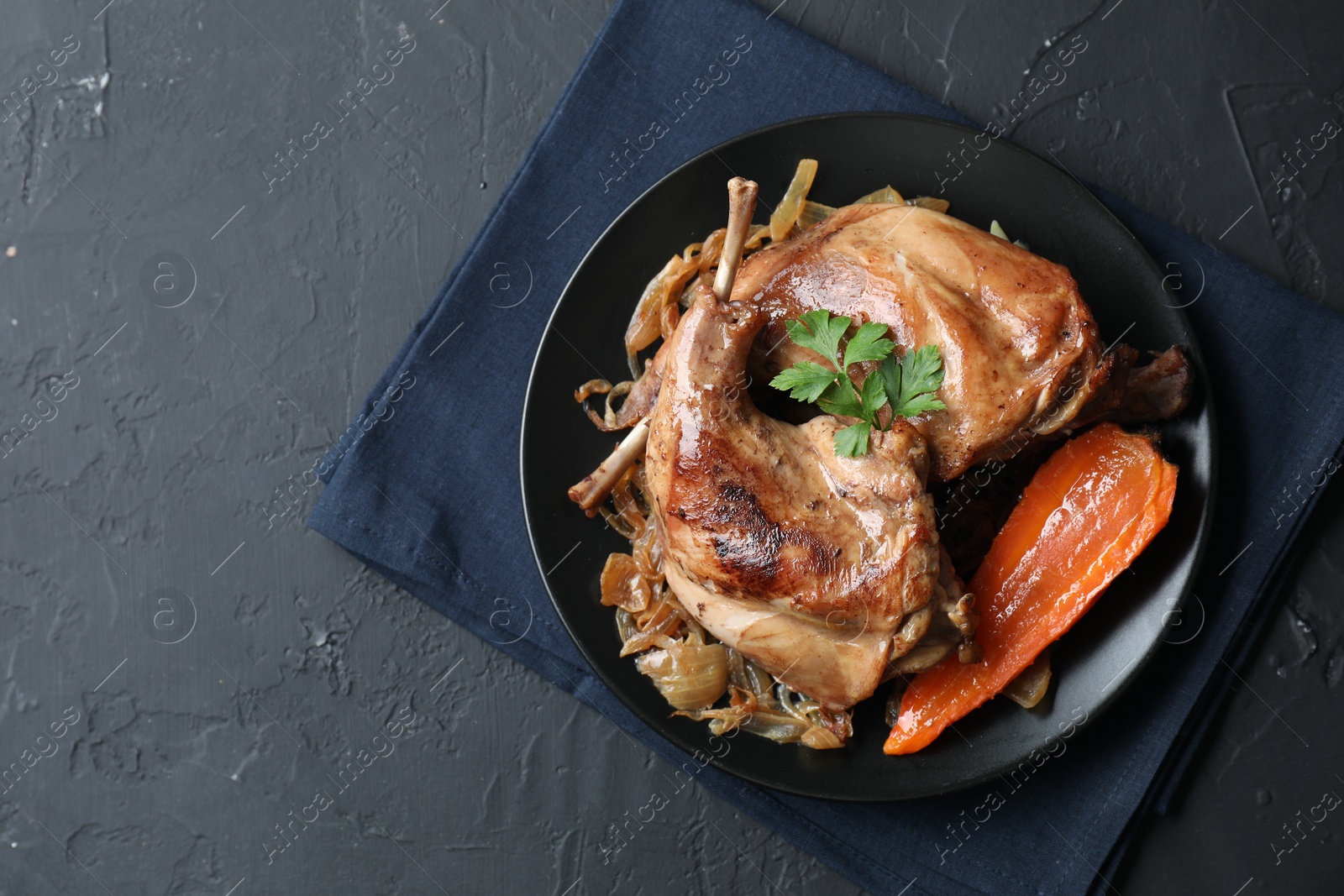 Photo of Tasty cooked rabbit meat with vegetables and parsley on black table, top view. Space for text