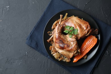 Photo of Tasty cooked rabbit meat with vegetables and parsley on black table, top view. Space for text