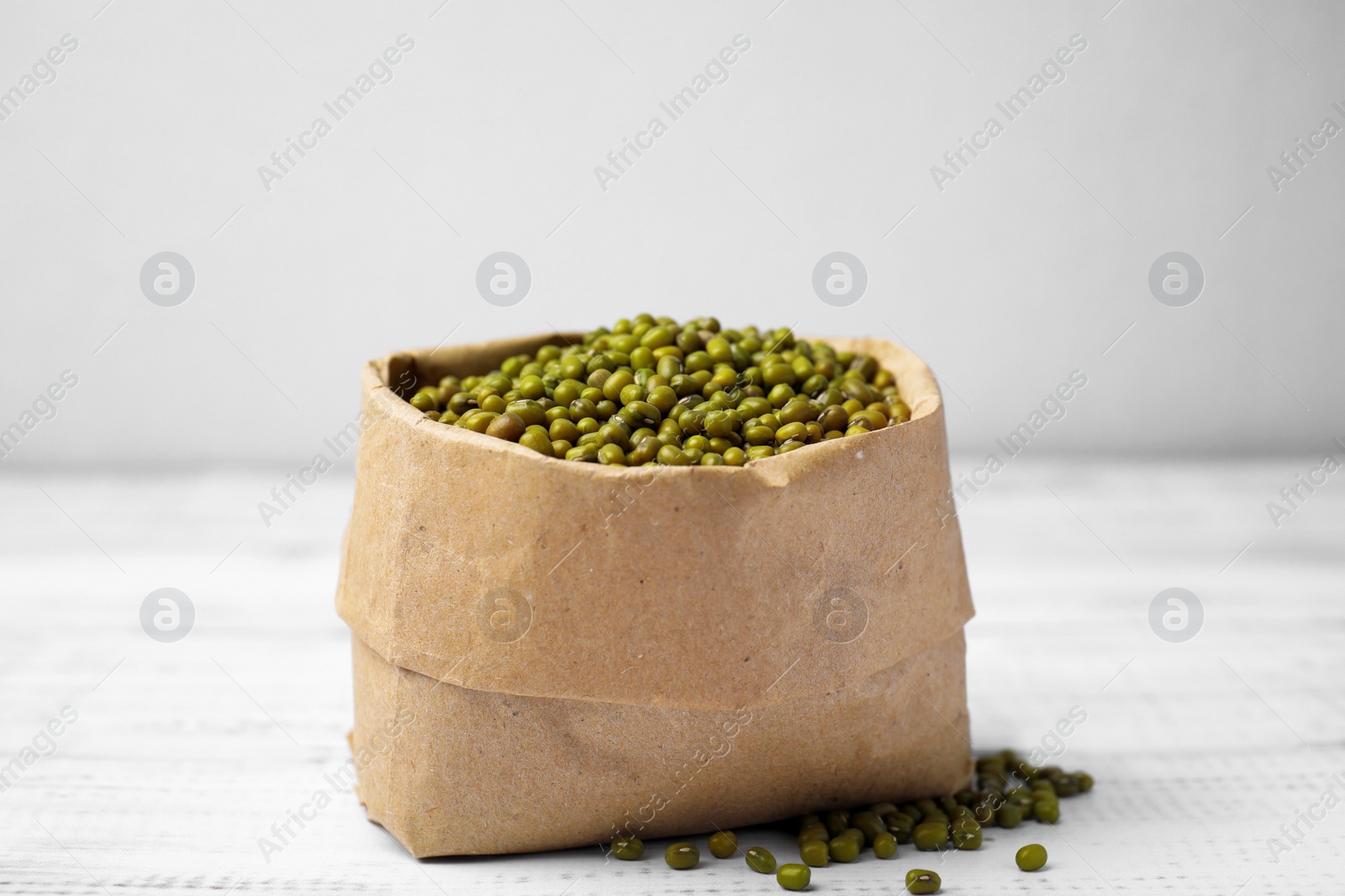 Photo of Paper bag with green mung beans on white wooden table