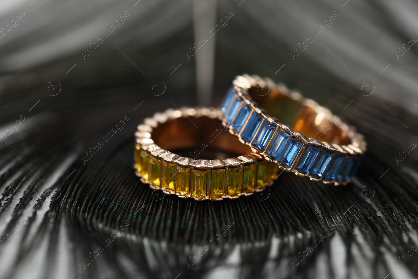 Photo of Two stylish rings and black feather on table, closeup