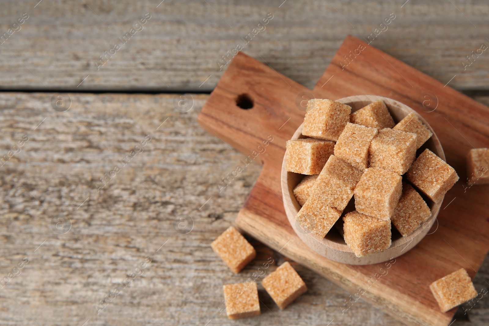 Photo of Bowl with brown sugar cubes on wooden table, above view. Space for text