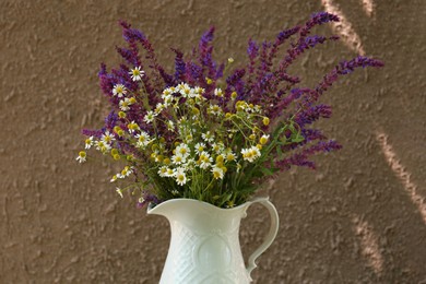 Photo of Beautiful bouquet with field flowers in jug near brown wall
