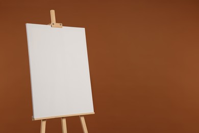 Photo of Wooden easel with blank canvas on brown background. Space for text