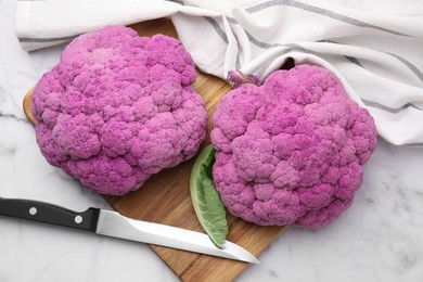 Photo of Fresh cauliflowers, cutting board and knife on white marble table, flat lay