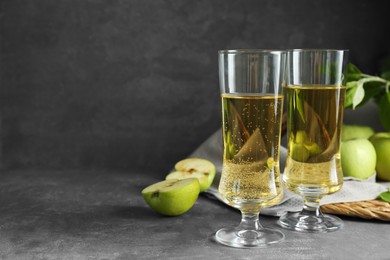 Photo of Glasses of delicious cider and green apples on gray table, space for text
