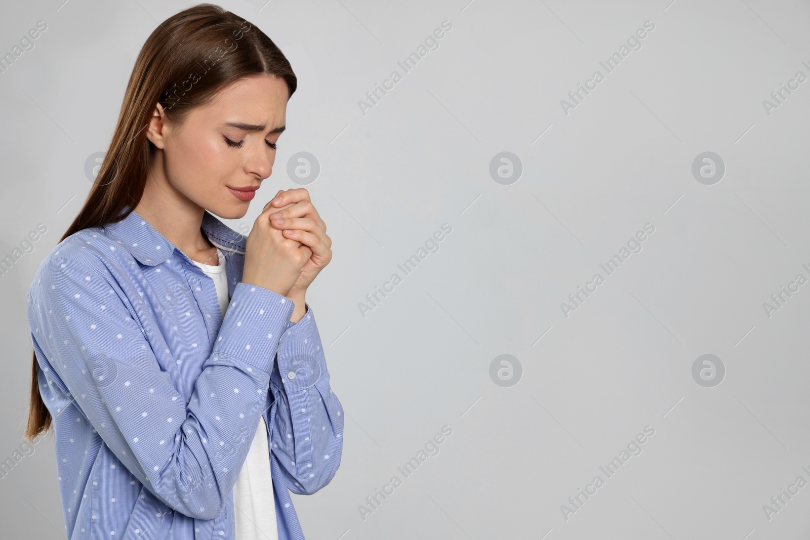 Photo of Woman with clasped hands praying on light grey background, space for text