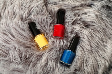 Photo of Bright nail polishes in bottles on grey faux fur, top view