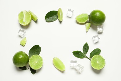 Frame made of ripe limes with green leaves and ice cubes on white background, flat lay