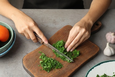 Photo of Woman cutting fresh green parsley on wooden board, closeup