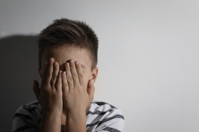 Photo of Scared little boy closing his eyes near white wall, space for text. Domestic violence concept