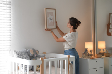 Photo of Decorator hanging picture on wall in baby room. Interior design
