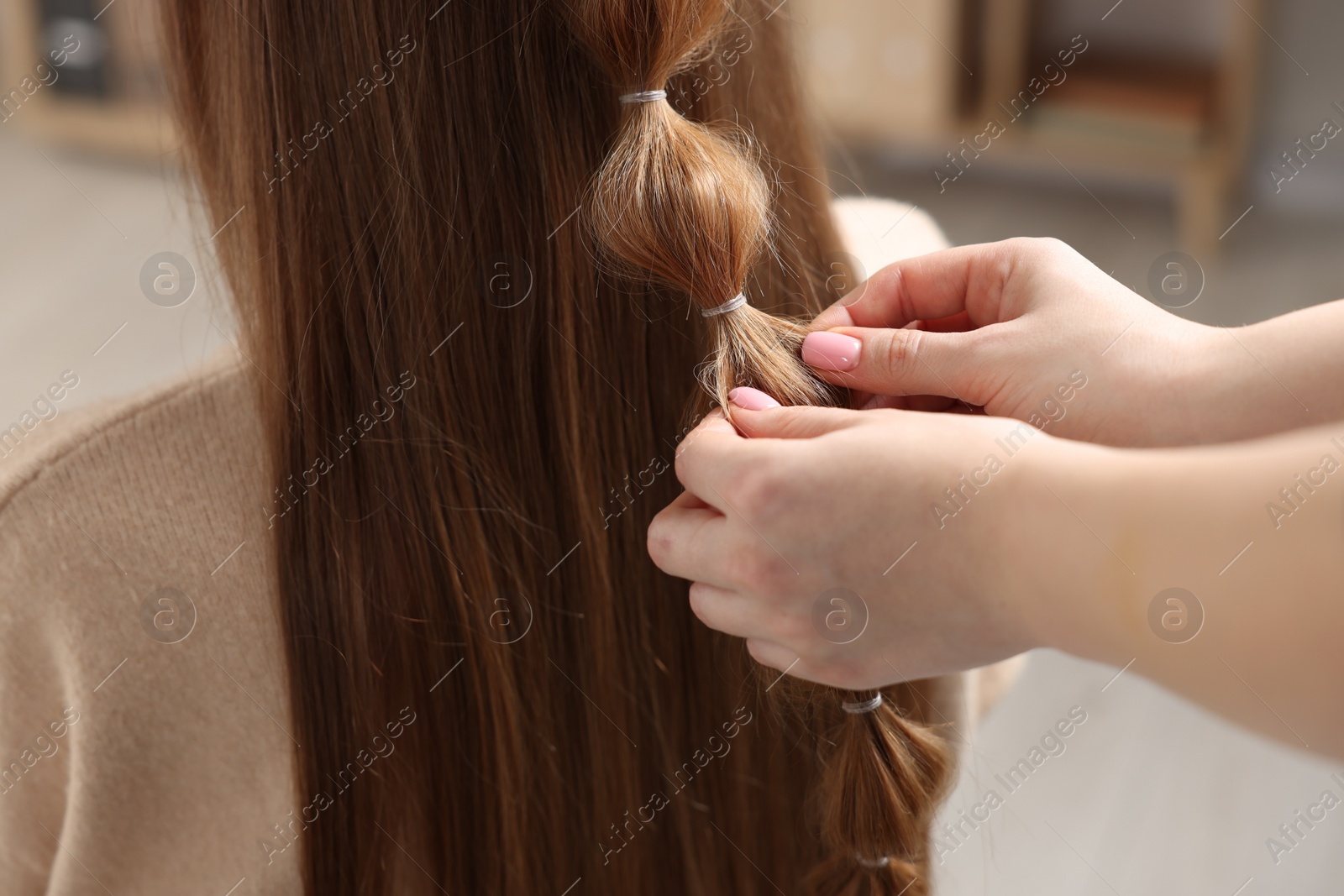 Photo of Professional stylist braiding woman's hair indoors, closeup