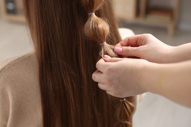 Professional stylist braiding woman's hair indoors, closeup