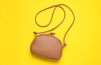 Stylish leather handbag on yellow background, top view
