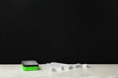 Photo of Pieces of chalk and duster on table near blackboard