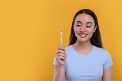 Photo of Happy young woman holding plastic toothbrush on yellow background, space for text