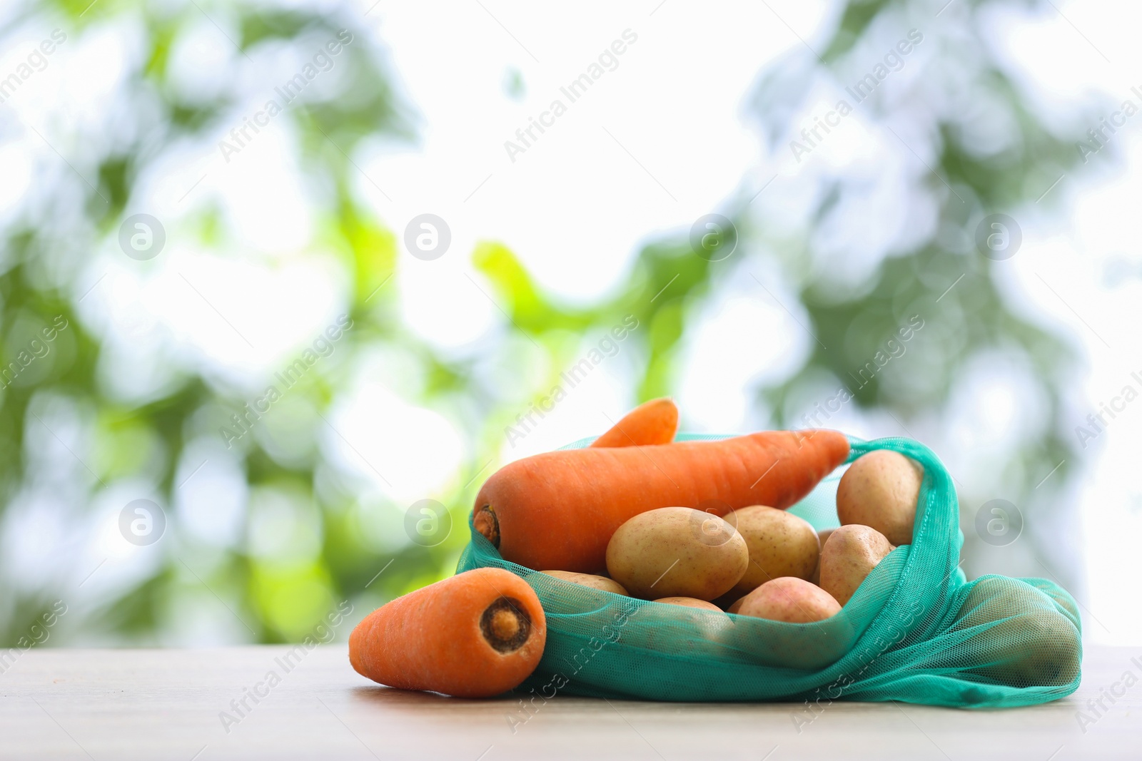 Photo of Net bag with vegetables on table against blurred background, space for text