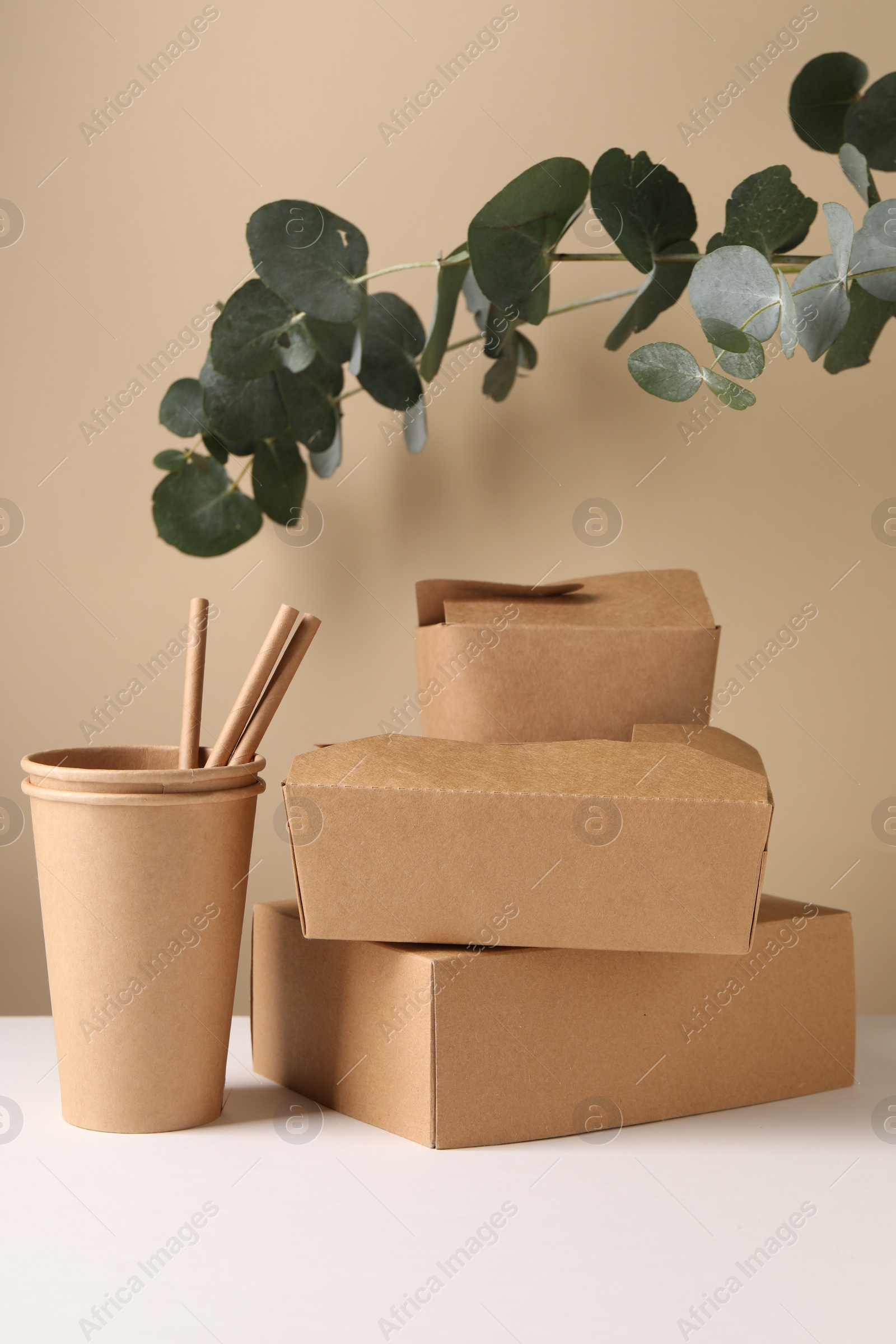 Photo of Eco friendly food packaging. Paper containers, straws and eucalyptus branches on white table against beige background