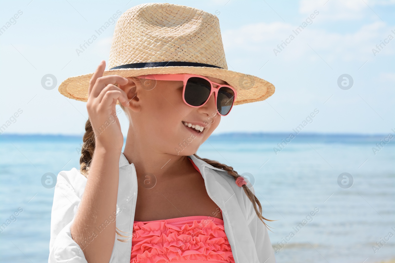 Photo of Little girl wearing sunglasses and hat at beach on sunny day