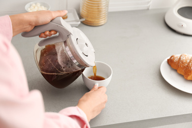 Photo of Woman pouring coffee into cup at home, closeup. Morning routine