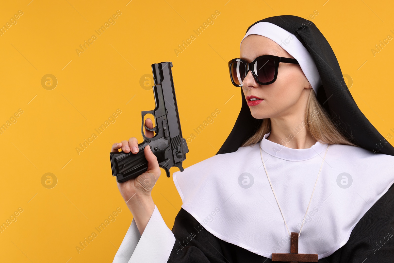 Photo of Woman in nun habit and sunglasses holding handgun against orange background, space for text