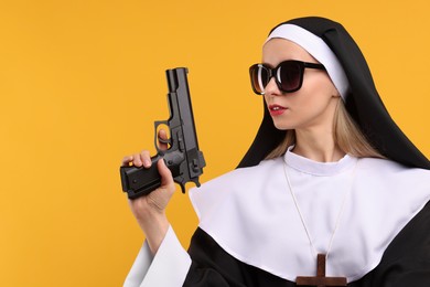 Woman in nun habit and sunglasses holding handgun against orange background, space for text