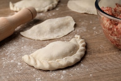 Photo of Uncooked chebureki, minced meat and rolling pin on wooden table, closeup
