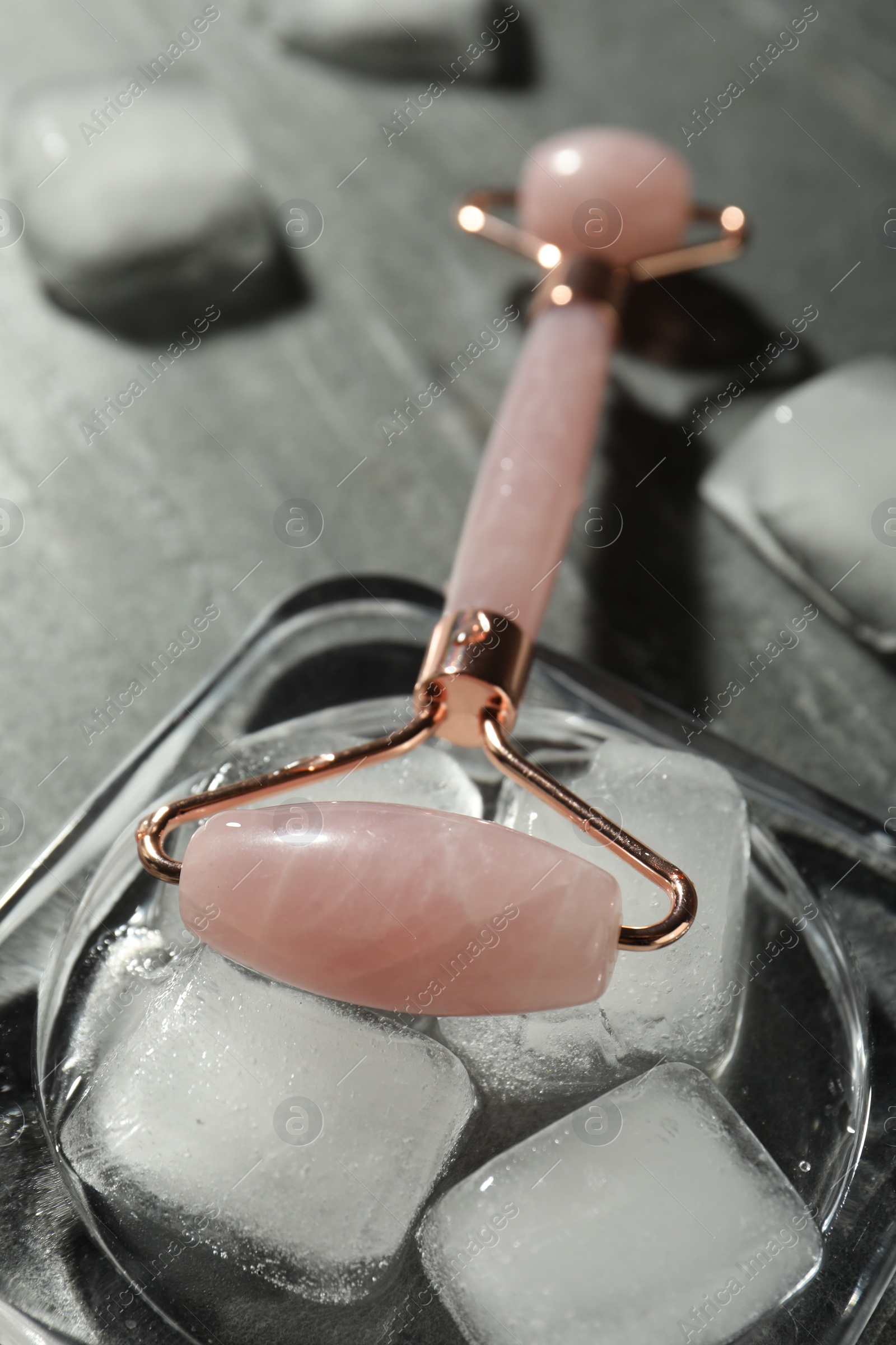 Photo of Natural jade face roller and ice cubes on grey background, closeup