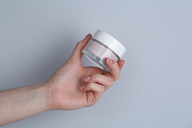 Woman holding jar of cream on grey background, closeup