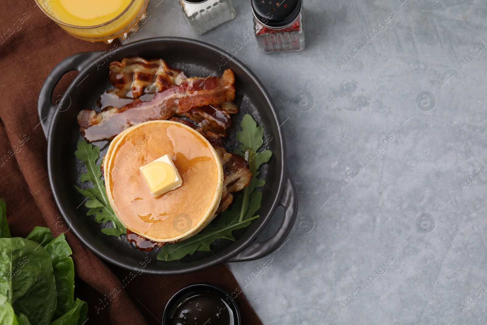 Photo of Tasty pancakes with butter, fried bacon and fresh arugula on grey table, flat lay. Space for text