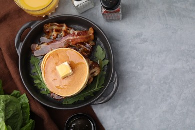 Tasty pancakes with butter, fried bacon and fresh arugula on grey table, flat lay. Space for text