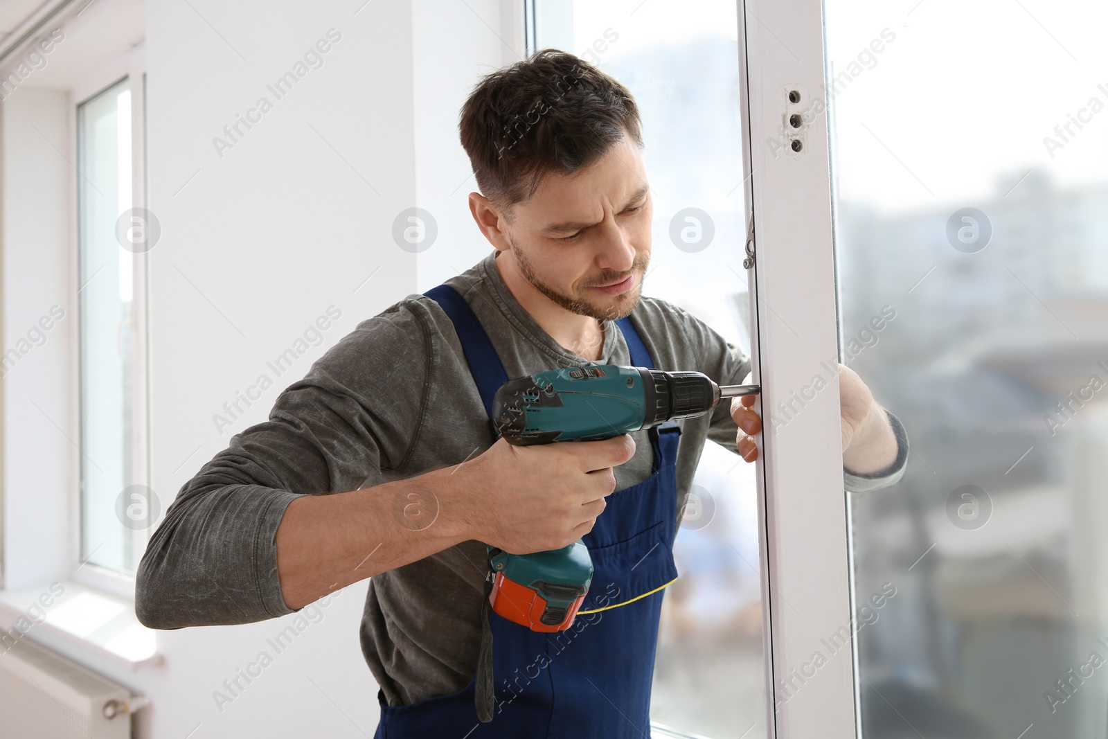 Photo of Construction worker using drill while installing window indoors