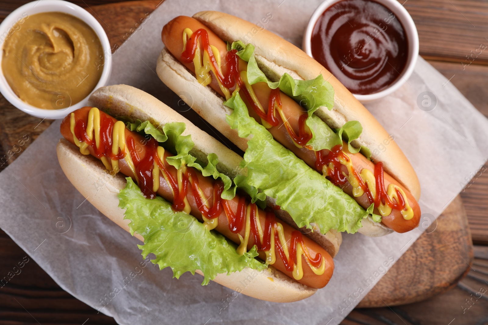 Photo of Tasty hot dogs with lettuce, ketchup and mustard on wooden table, top view