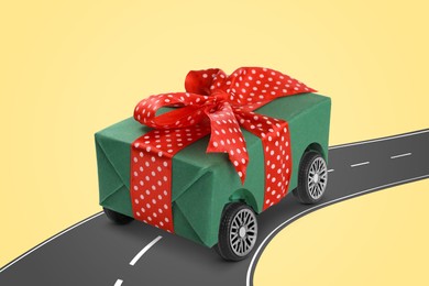 Gift box with wheels riding on asphalt road against pale yellow background. Delivery service