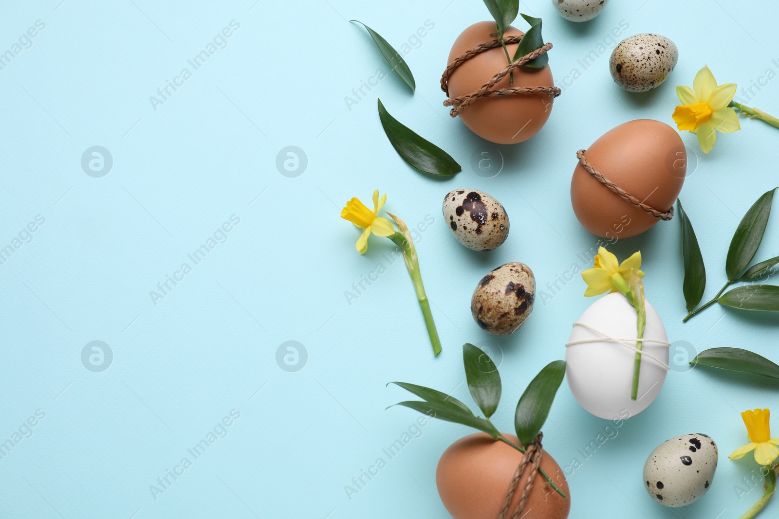 Photo of Easter eggs decorated with green leaves and flowers on light blue background, flat lay. Space for text